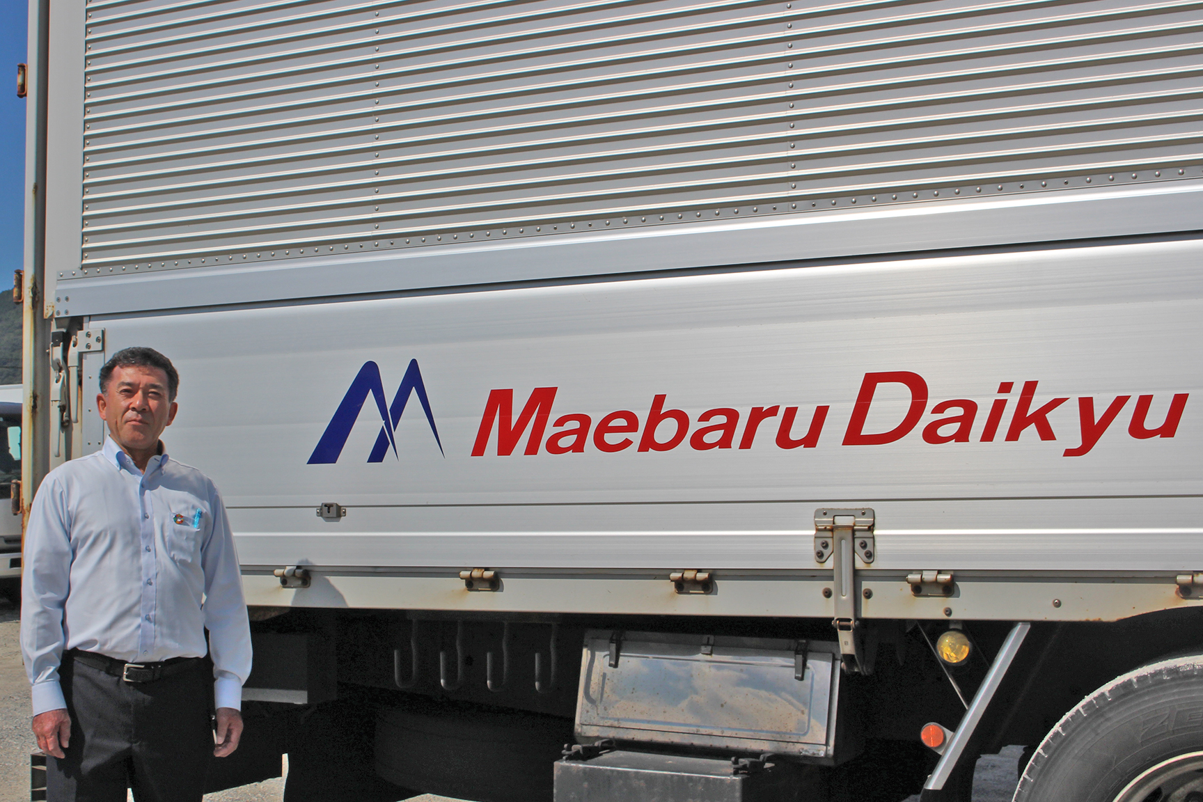 本社に並ぶ運送用トラックと関口社長